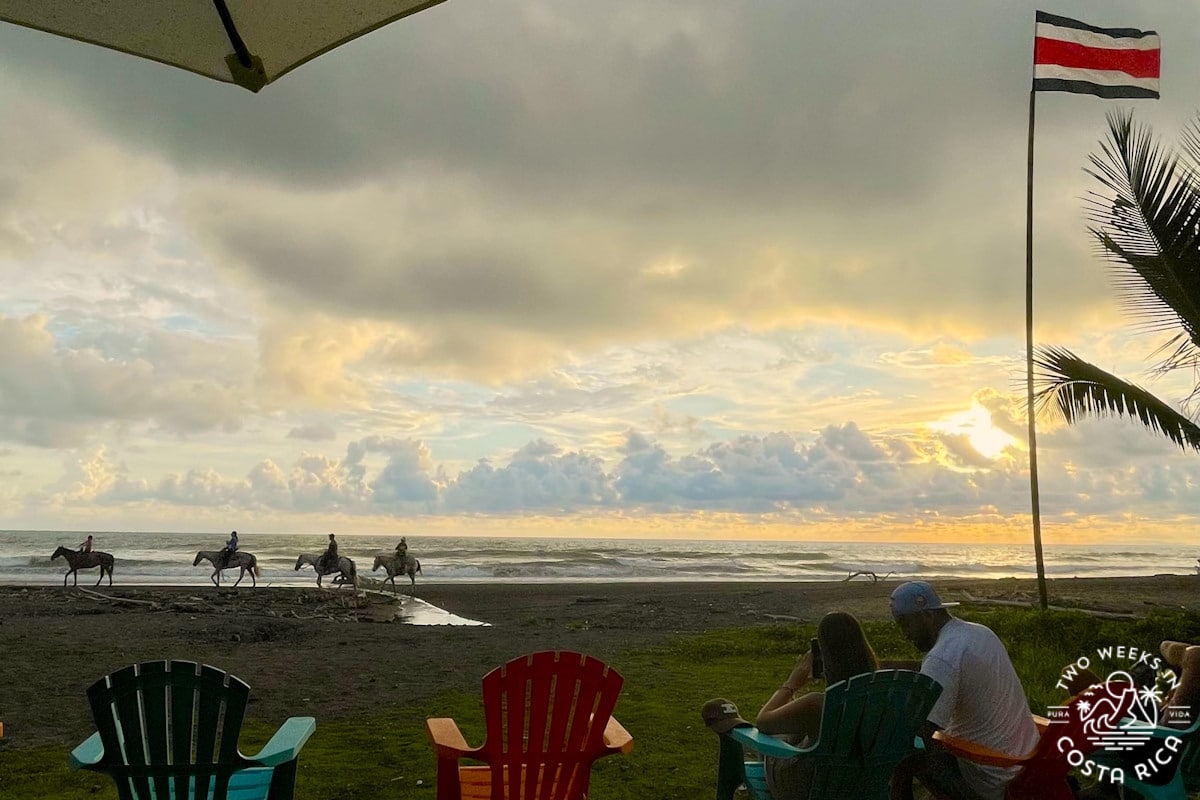 Cloudy sunset at the beach with horseback riders passing by and people sitting in beach chairs