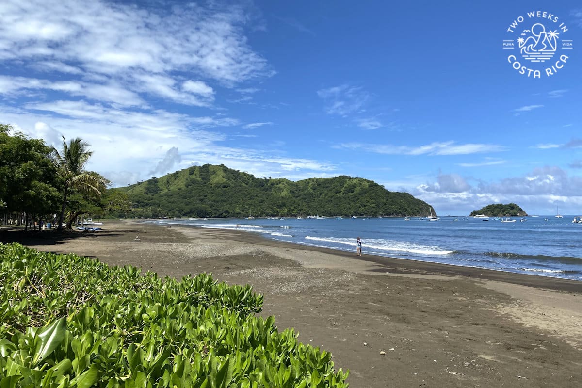 A brown sand beach with ocean and small mountain in the background