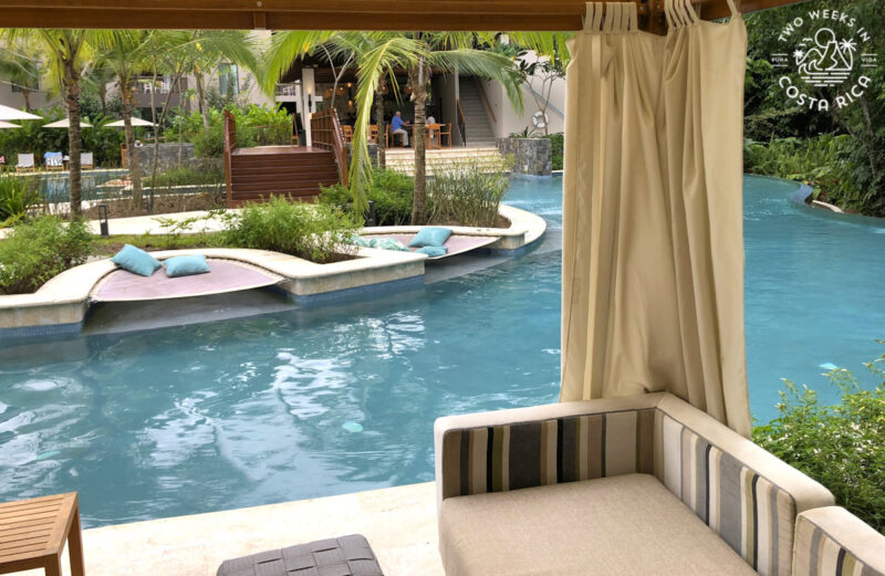 a poolside cabana with tropical plants and palm trees in the background