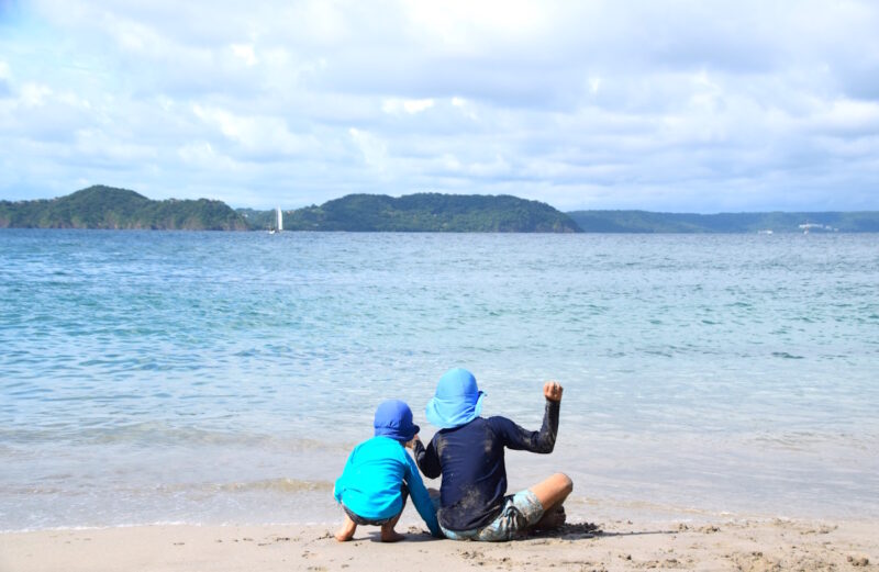 two kids sitting on the sand at the beach in costa rica