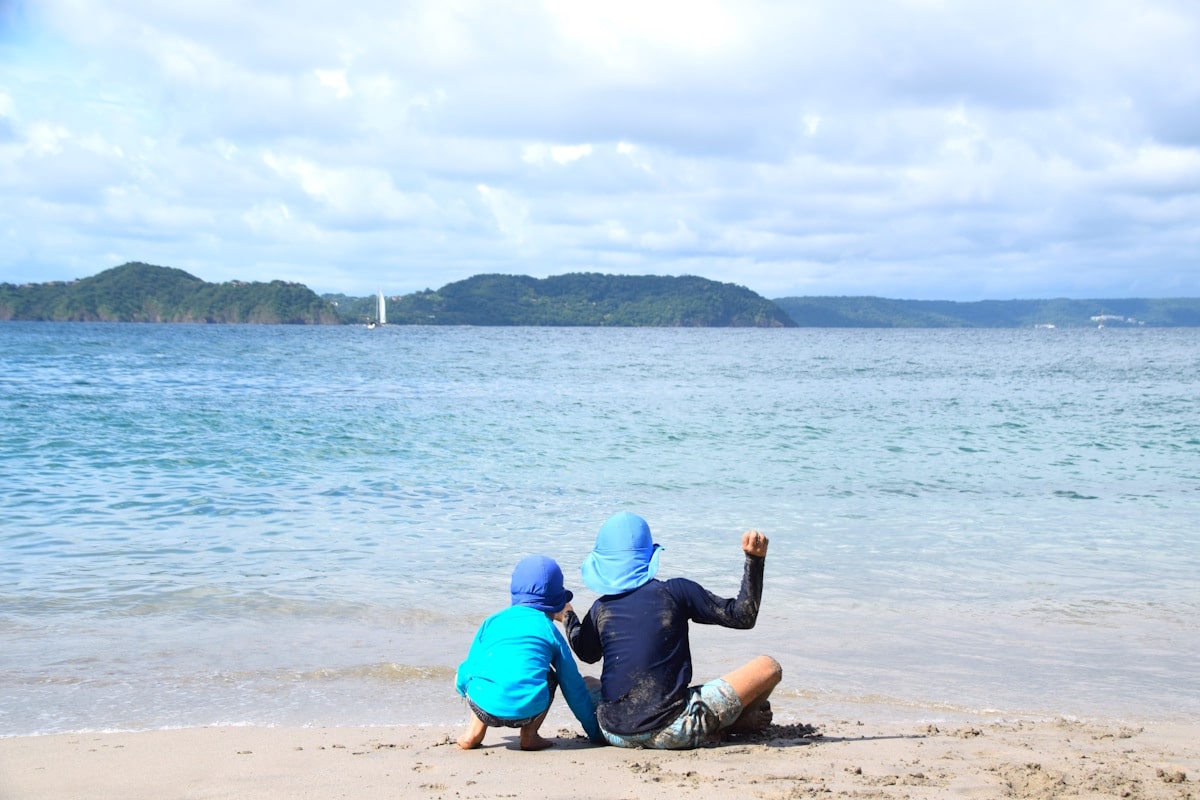 two kids sitting on the sand at the beach in costa rica