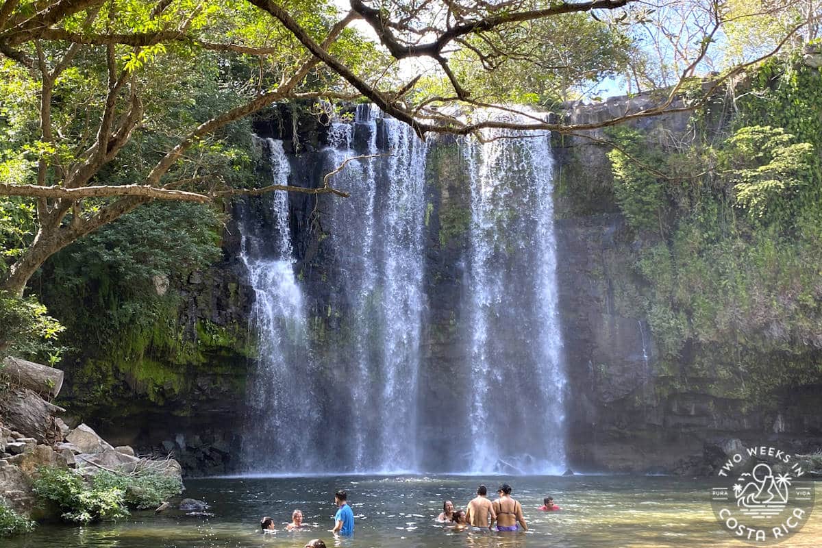 people swimming in a shallow waterfall pool