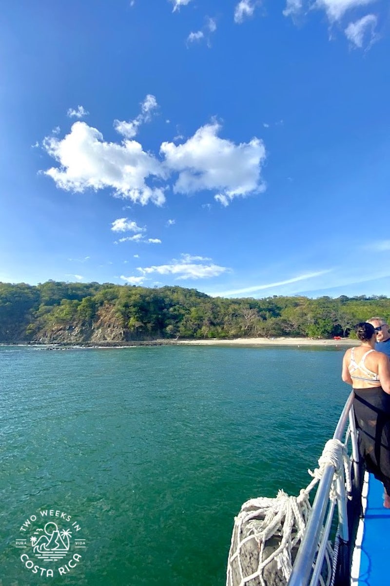 person on a boat lookin gout at the green sea with a white beach in the distance
