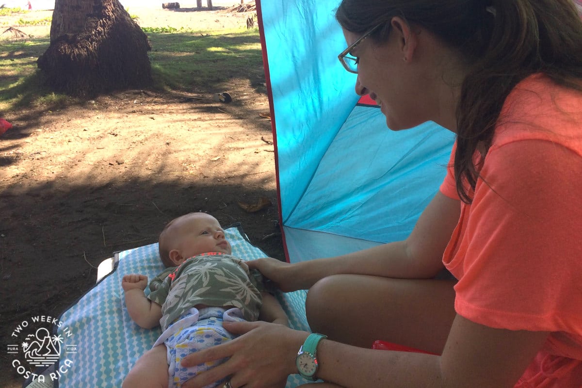 a mom changing a baby's diaper on the beach in costa rica