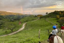 People horseback riding on a mountain ridge with a rainbow in the distance
