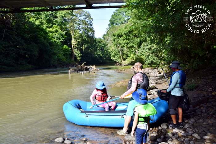 A woman sitting in a rubber raft holding a paddle with others waiting to get in during a river float tour La Fortuna