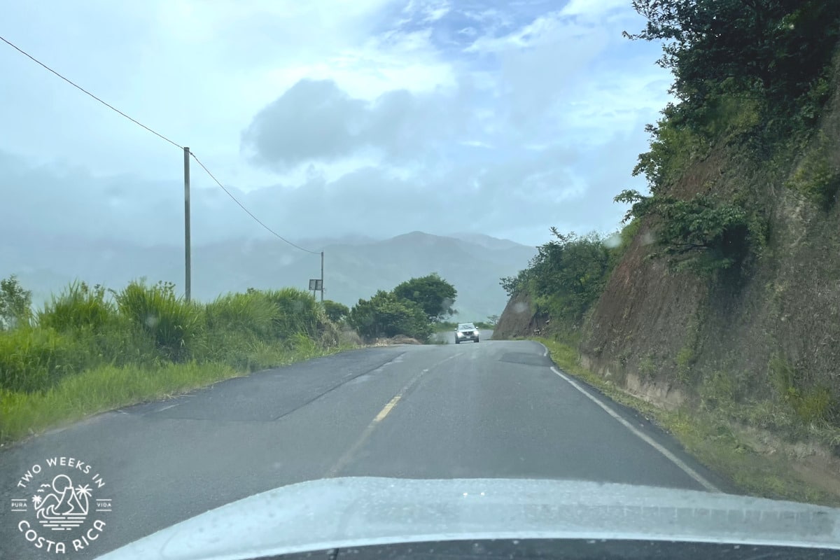 A paved road with a large cliff on one side and mountains in the distance
