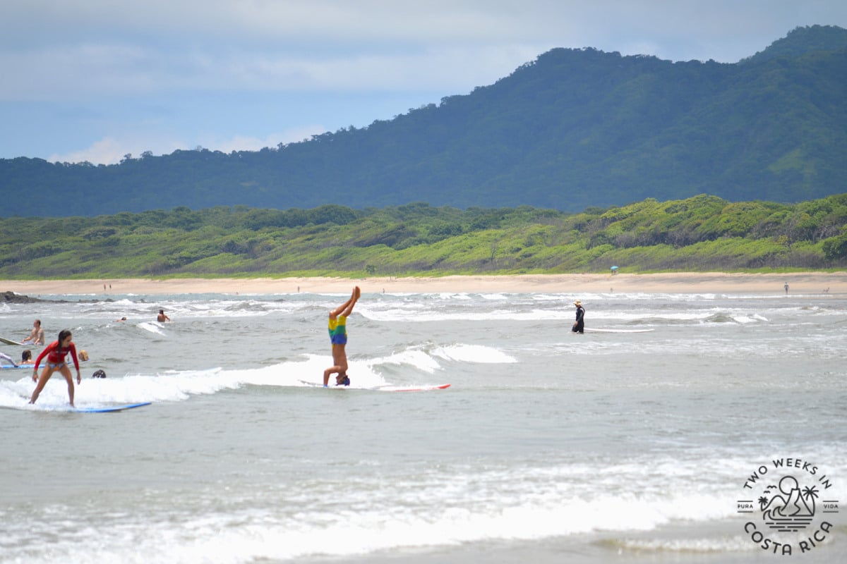 Several surfers riding waves at Tamarindo Beach, one is doing a handstand on the surfboard