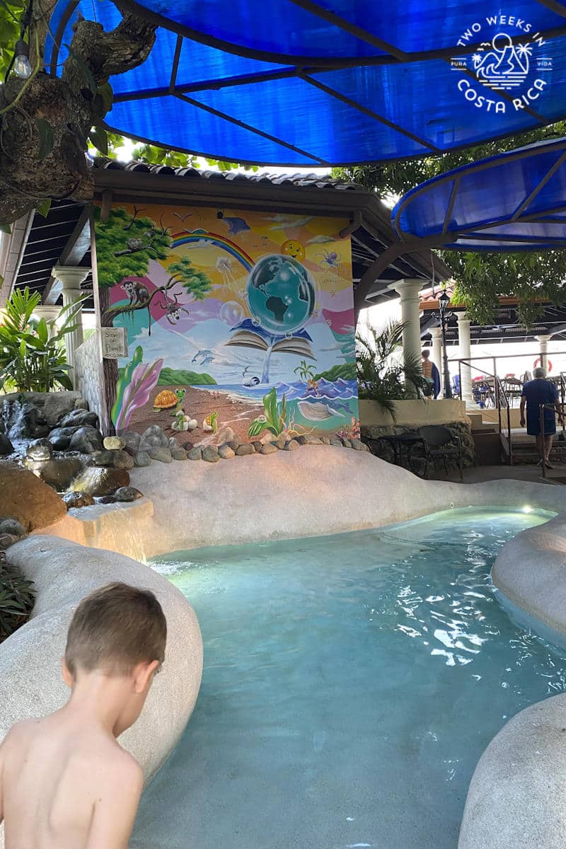 child walking into a shallow pool with a mural on the wall