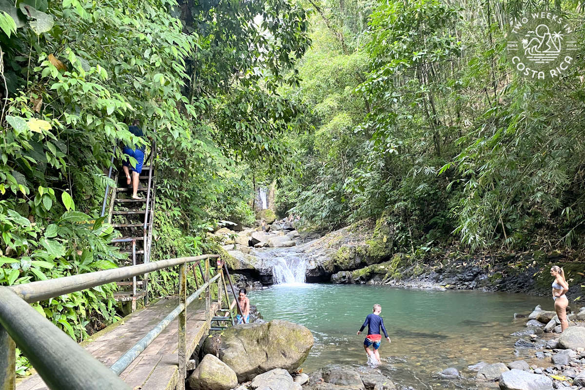platform next to a river and waterfall with people swimming