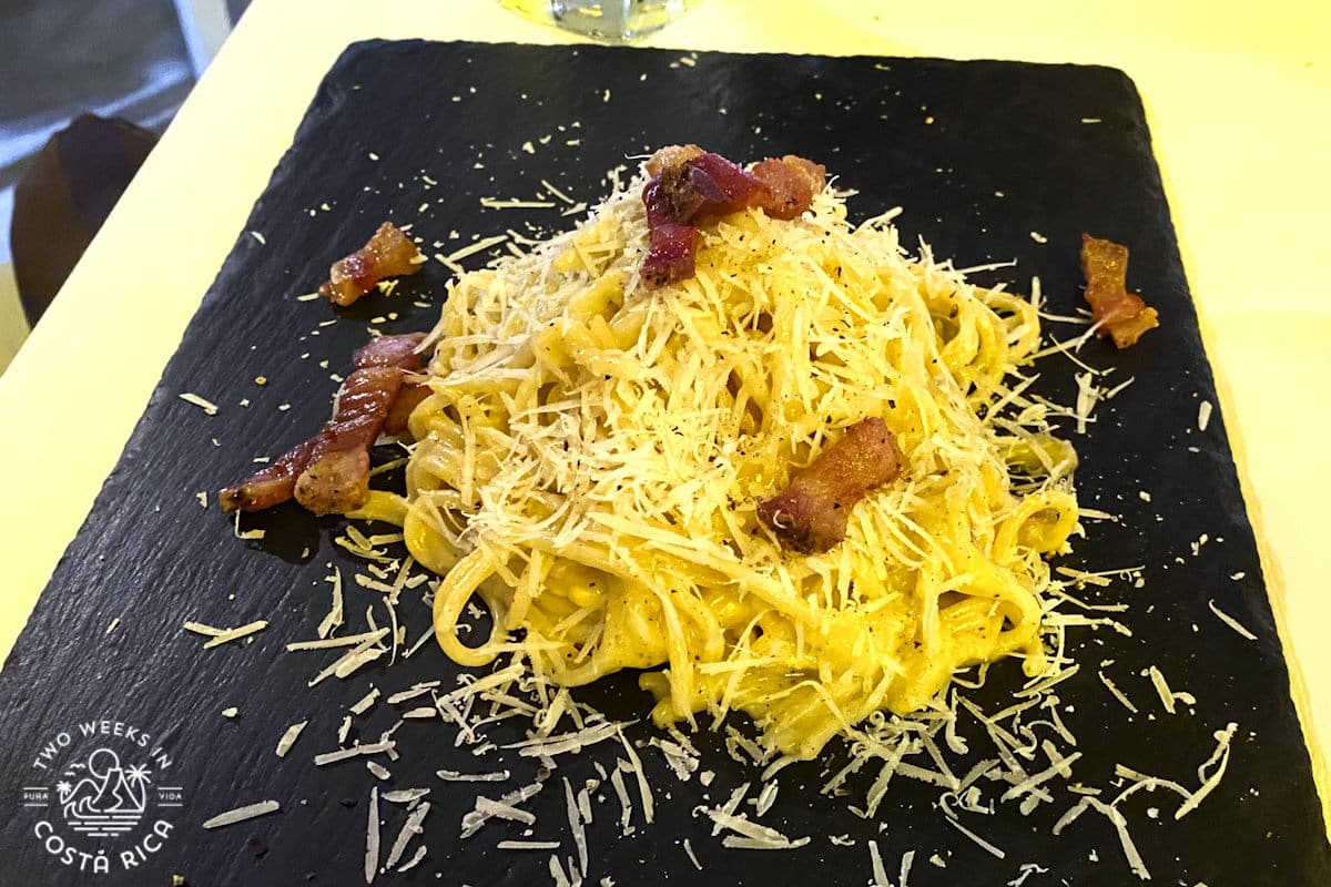 Pasta with bacon and shredded cheese served on a black slate