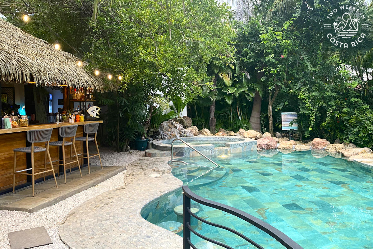 a pool with green tile and a palm thatched bar